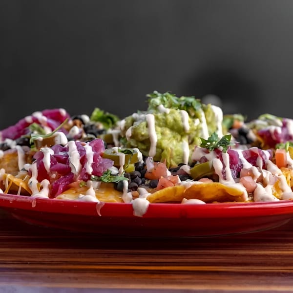 A vibrant plate of Mexicali Blue nachos, topped with guacamole, pickled onions, and a creamy drizzle.