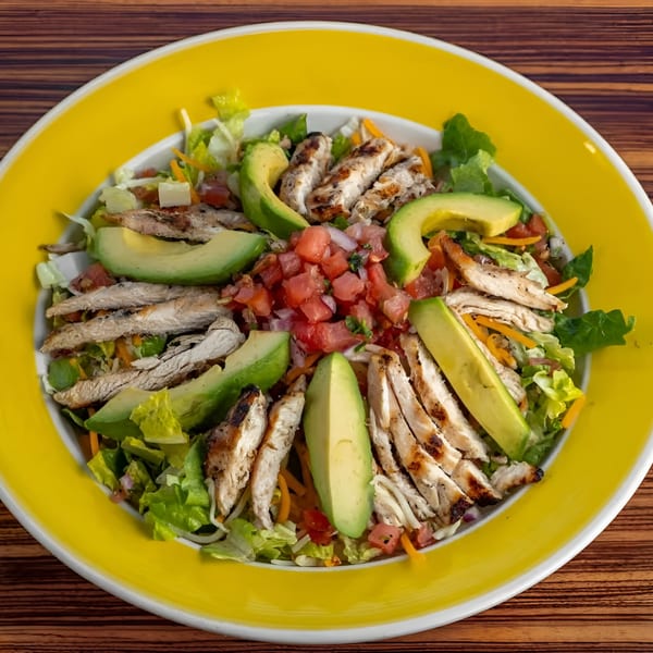 Grilled chicken salad with avocado slices, pico de gallo, and mixed greens in a yellow bowl.