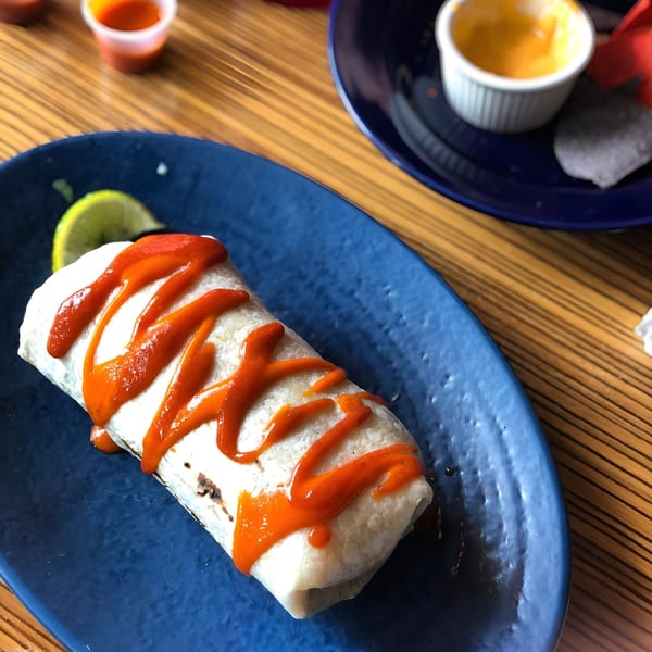 A Mexicali Blue burrito drizzled with red sauce, served on a blue plate with a lime wedge.