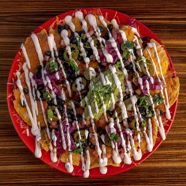 A vibrant red plate of Mexicali Blue nachos, topped with black beans, jalapenos, guacamole, and crema.