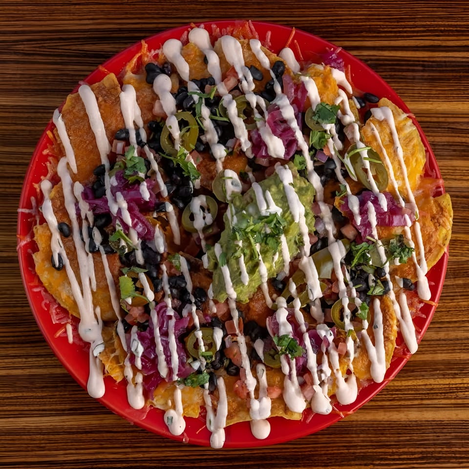 A vibrant red plate of Mexicali Blue nachos, topped with black beans, jalapenos, guacamole, and crema.