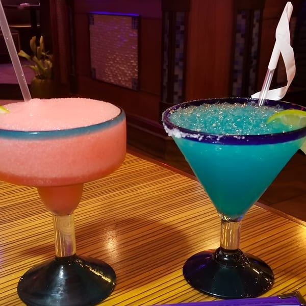 Two vibrant frozen margaritas, one pink and one blue, on a wooden table at Mexicali Blue.