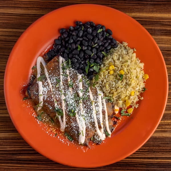 Mexicali Blue's enchiladas with black beans and rice, garnished with crema, cheese, and cilantro.