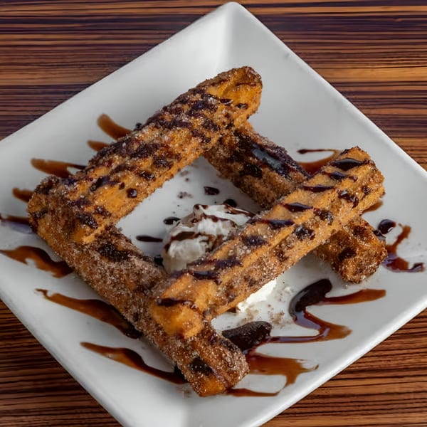 Four churros drizzled with chocolate sauce and sugar, with a scoop of vanilla ice cream.