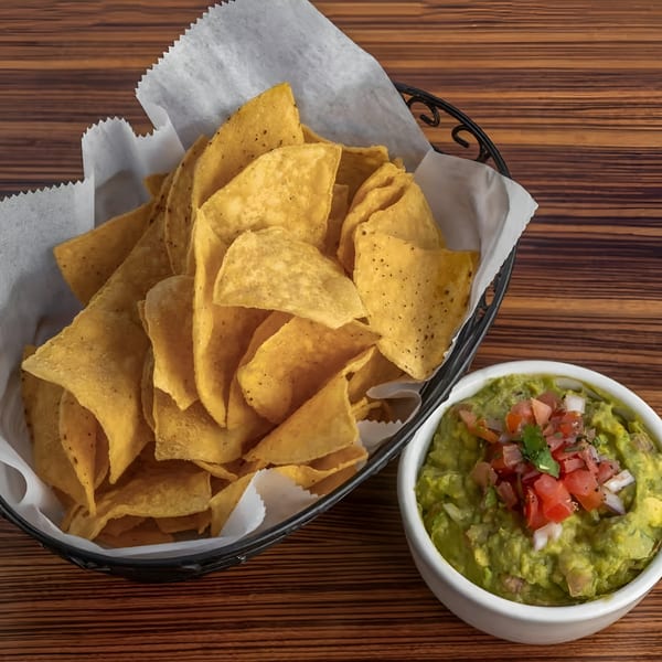 A basket of crispy tortilla chips next to a bowl of guacamole topped with pico de gallo.