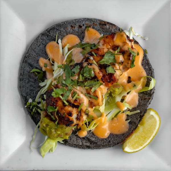 A Mexicali Blue shrimp taco on a blue corn tortilla with sauce, cilantro, and a lime wedge.